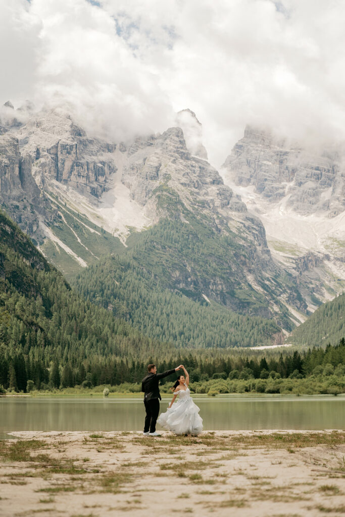 Couple dancing by mountain lake in wedding attire.