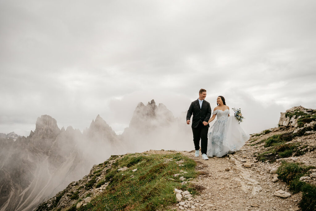 Couple walking on mountain path in wedding attire.