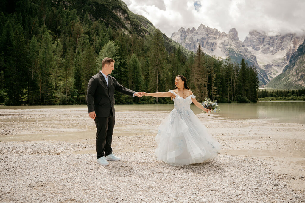 Bride and groom holding hands by mountain lake.