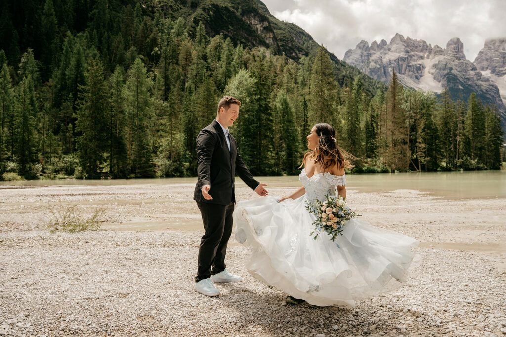 Bride and groom smiling by lakeside landscape.