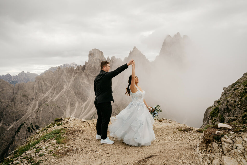 Couple dancing on a mountain cliff in wedding attire.