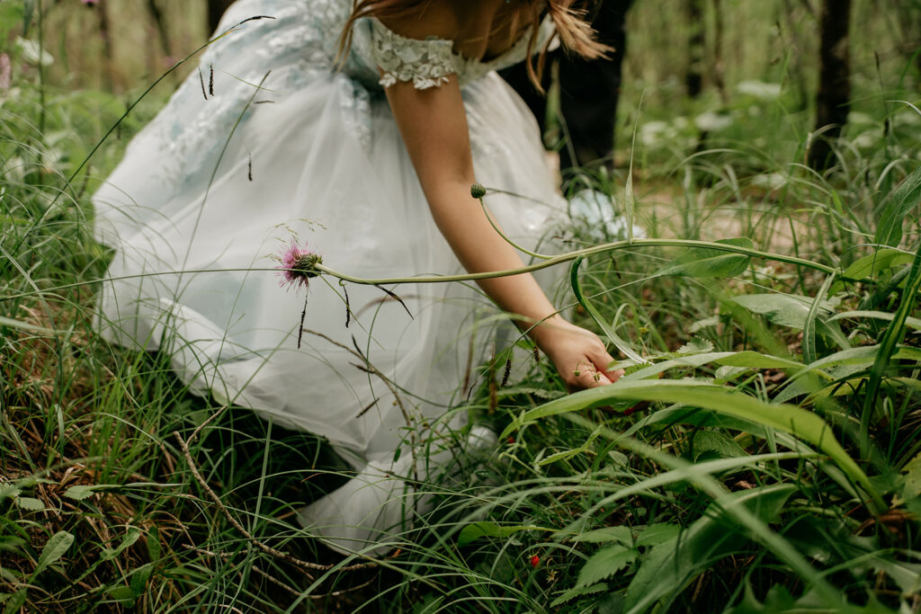 Child in white dress exploring forest greenery.