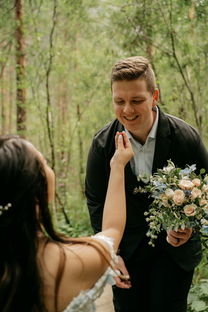 Smiling couple exchanging vows in forest setting.