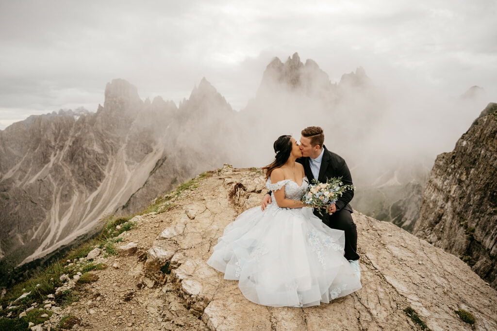 Bride and groom kissing on mountain peak.