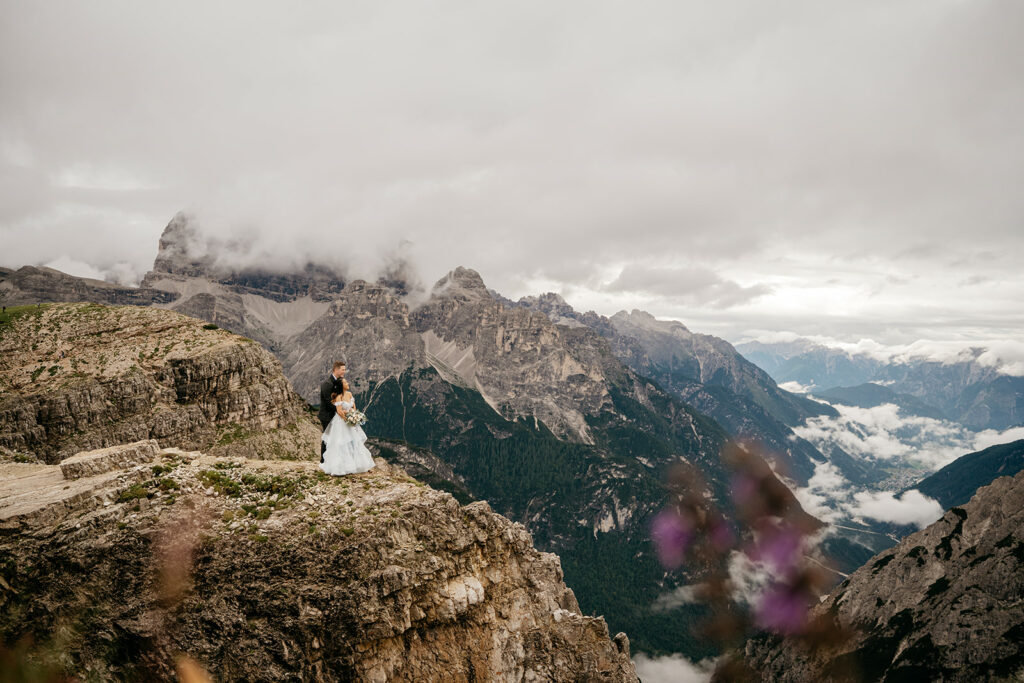 Couple embraces on mountain cliff with breathtaking view.