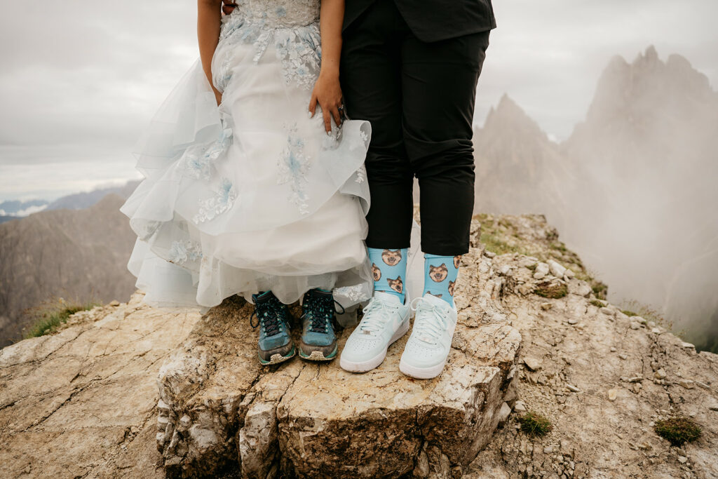 Bride and groom sneakers on rocky mountain ledge.