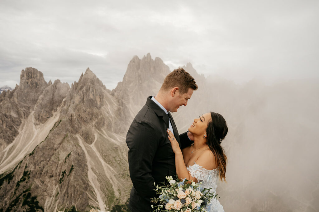Bride and groom embracing in mountain scenery.