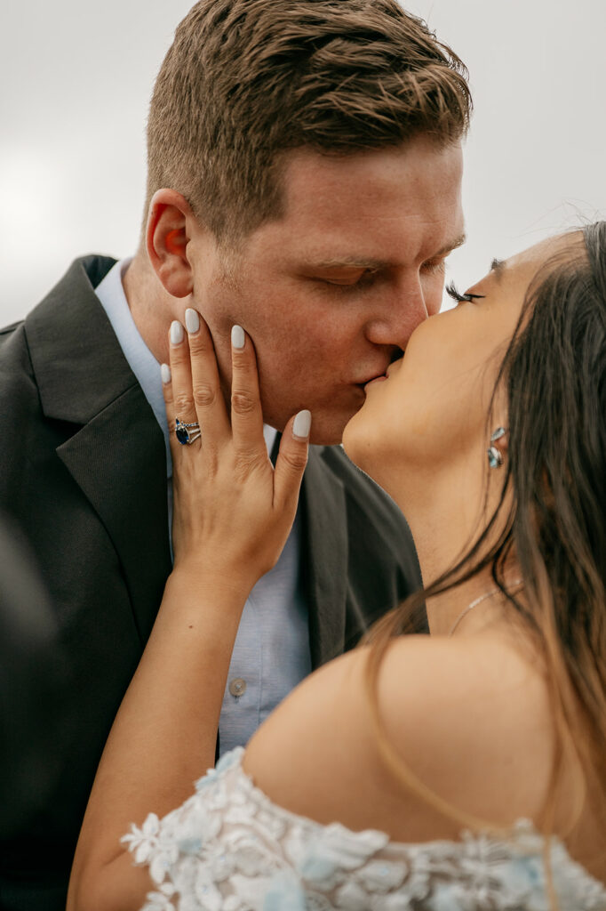 Couple kissing with engagement ring visible.