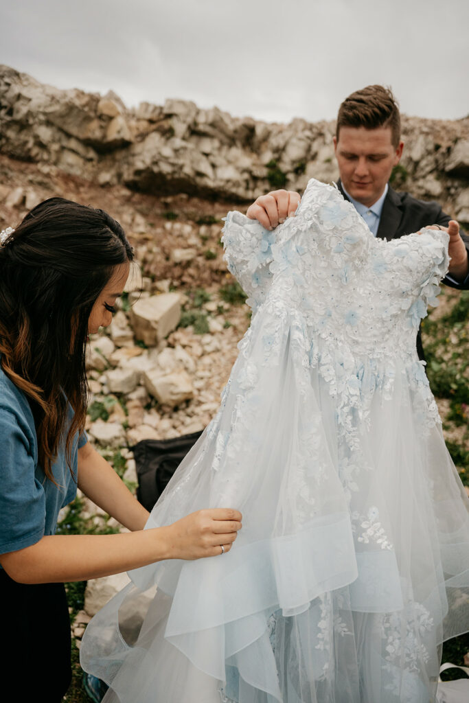 Two people holding an intricate, floral wedding dress.