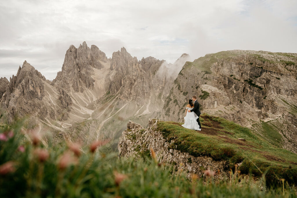 Couple embraces on mountain cliff with stunning view.
