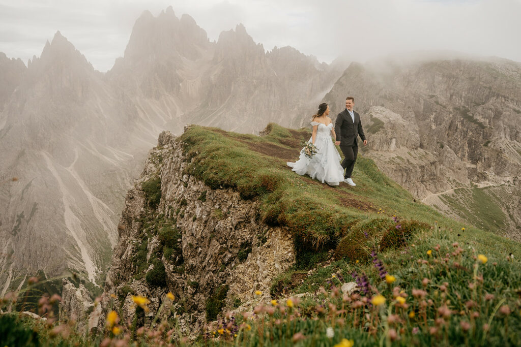 Couple in wedding attire on mountain cliff.