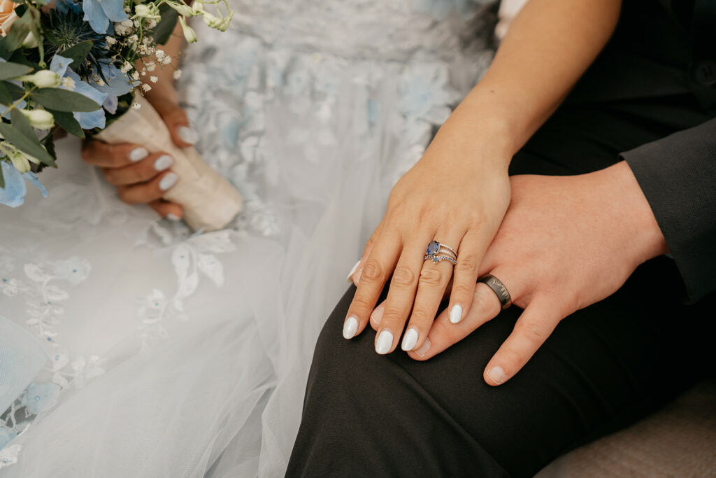Bride and groom holding hands with rings visible.