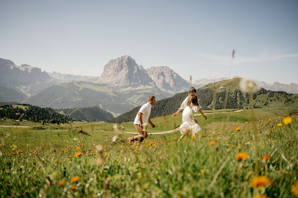 Couple running in meadow with mountain view.