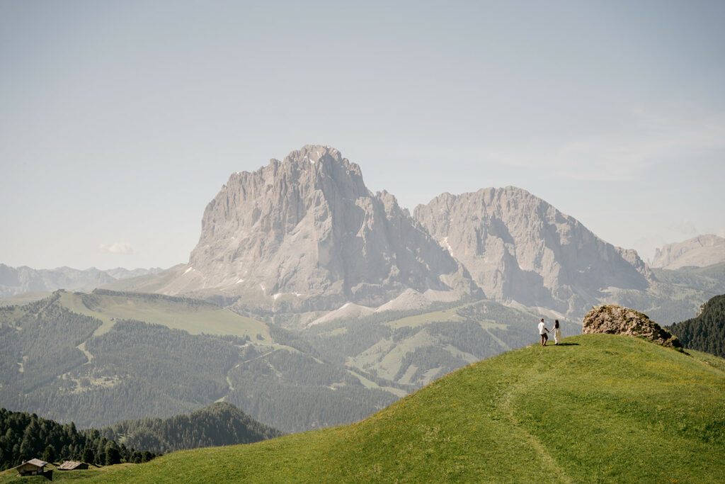 Couple walking on hillside near mountain landscape.