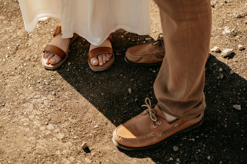 Couple's feet in sandals on rocky ground.