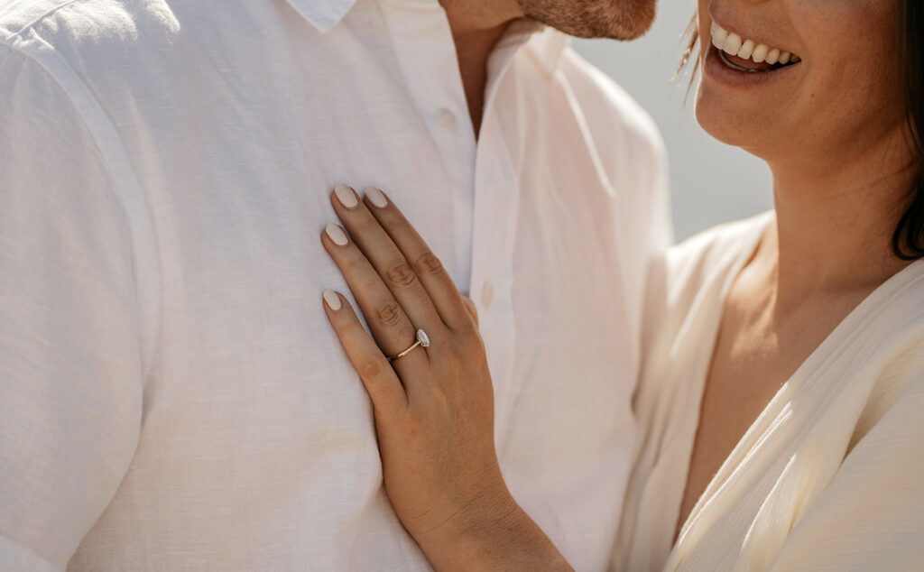 Close-up of smiling couple, engagement ring visible.
