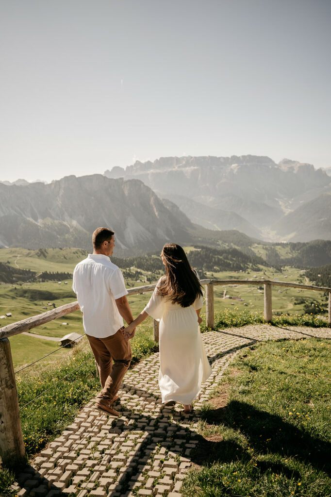 Couple holding hands, walking mountain path.