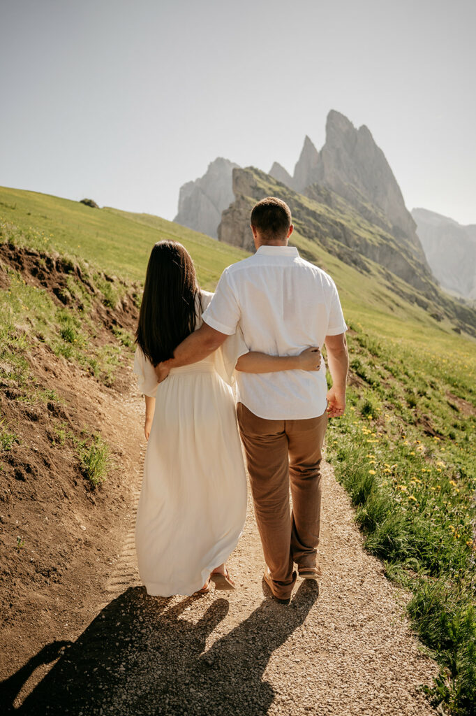 Couple walking on mountain path under clear sky.