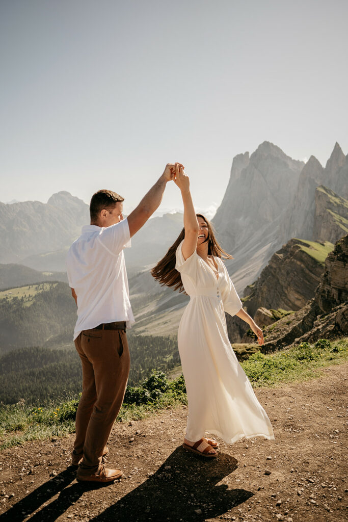 Couple dancing on mountain path with scenic view.