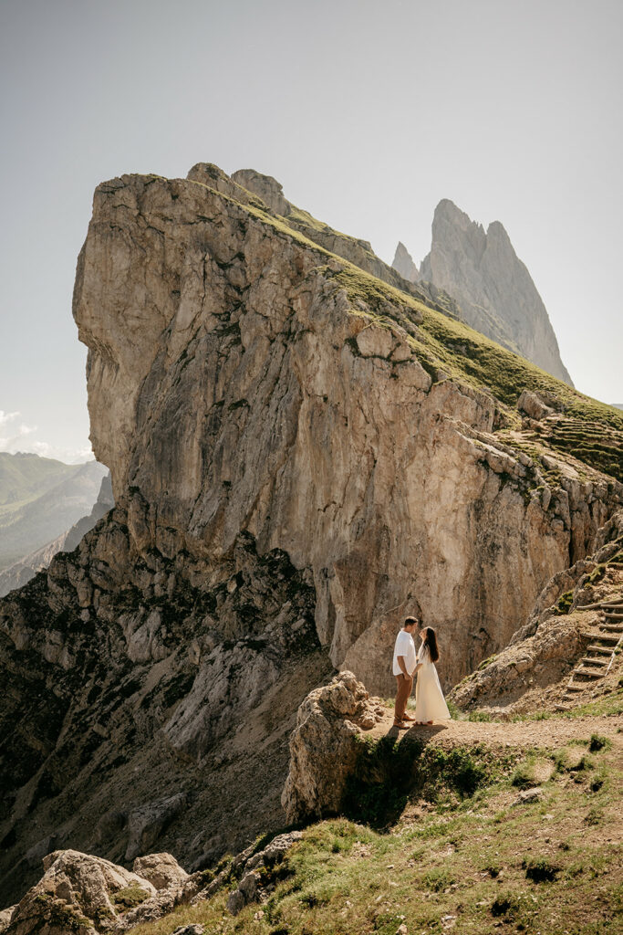 Couple standing on rocky mountain cliff, sunny day.