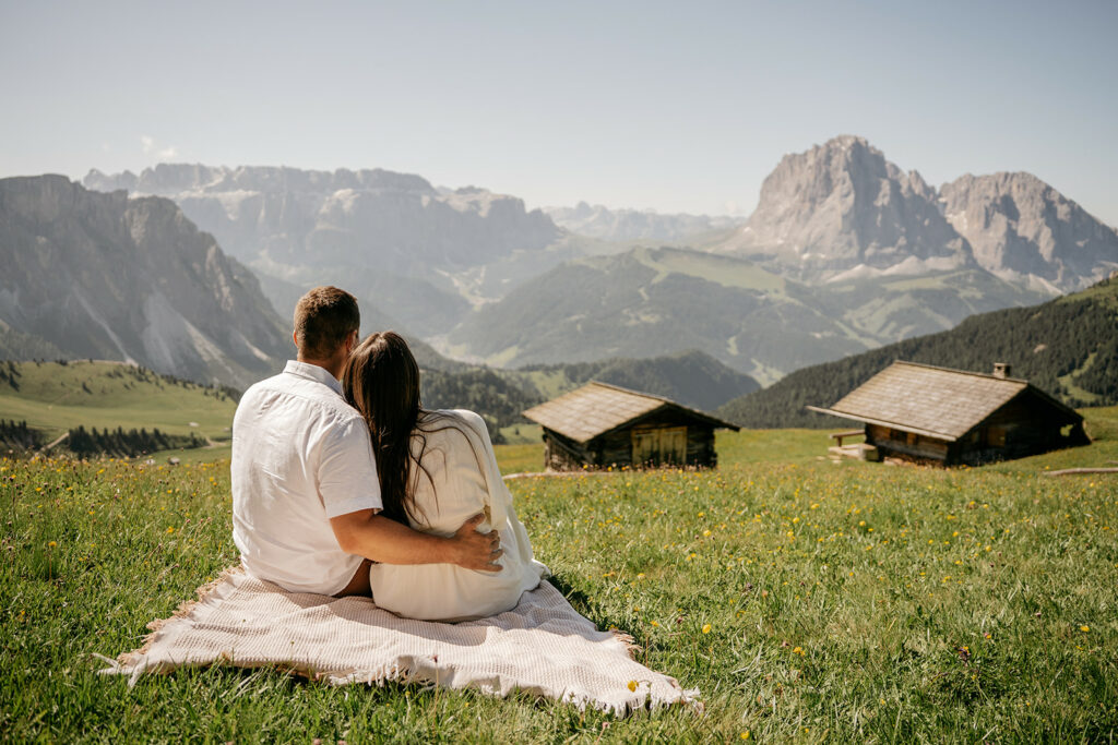 Couple sitting on blanket overlooking mountains and huts.