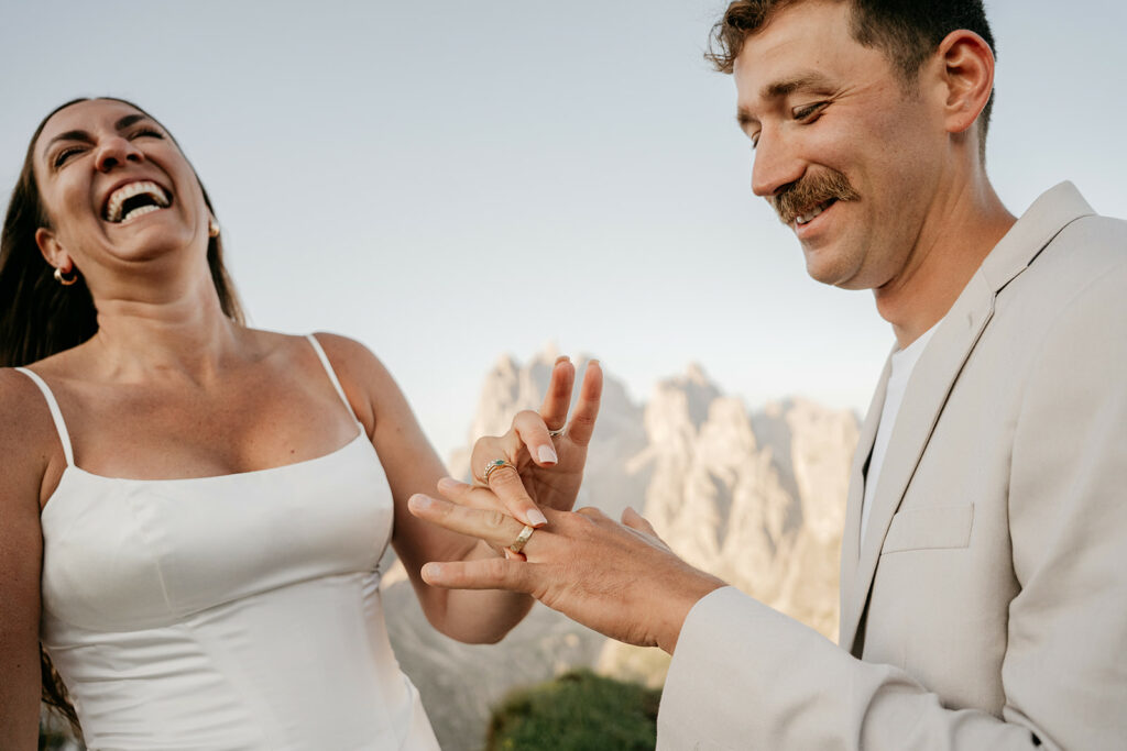 Couple exchanging rings outdoors, smiling.