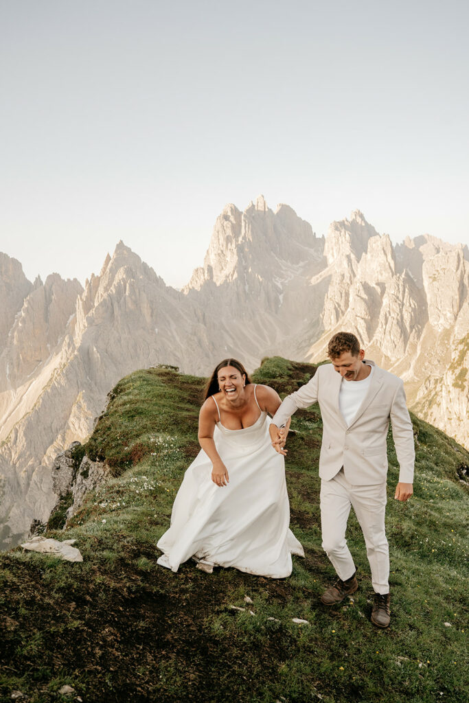 Couple laughing on mountain ridge in wedding attire.