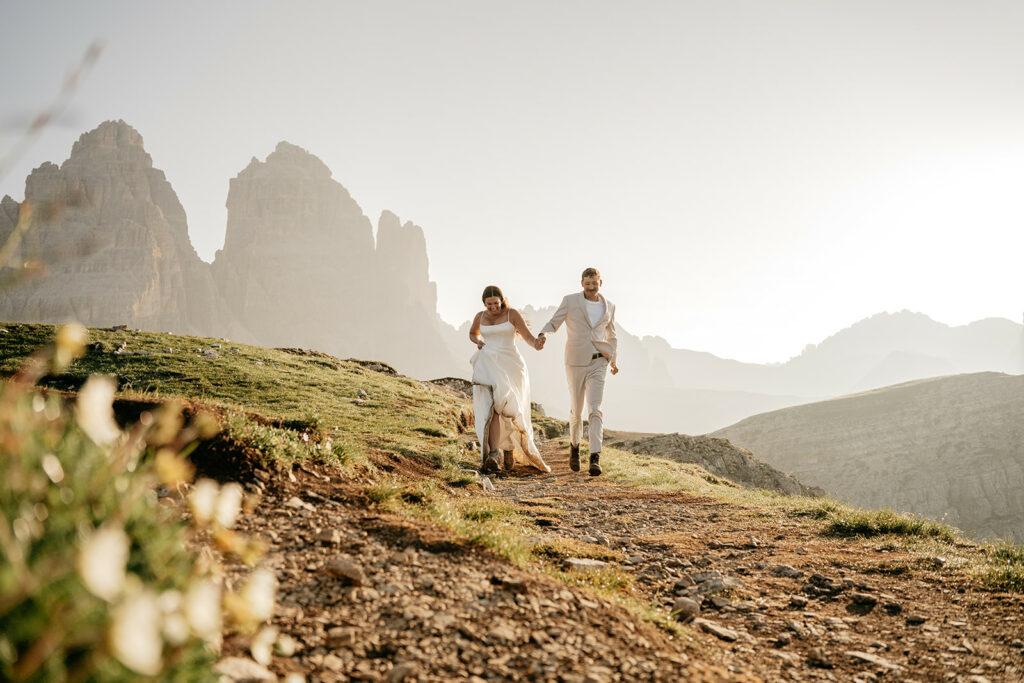 Couple in wedding attire walks mountain path.