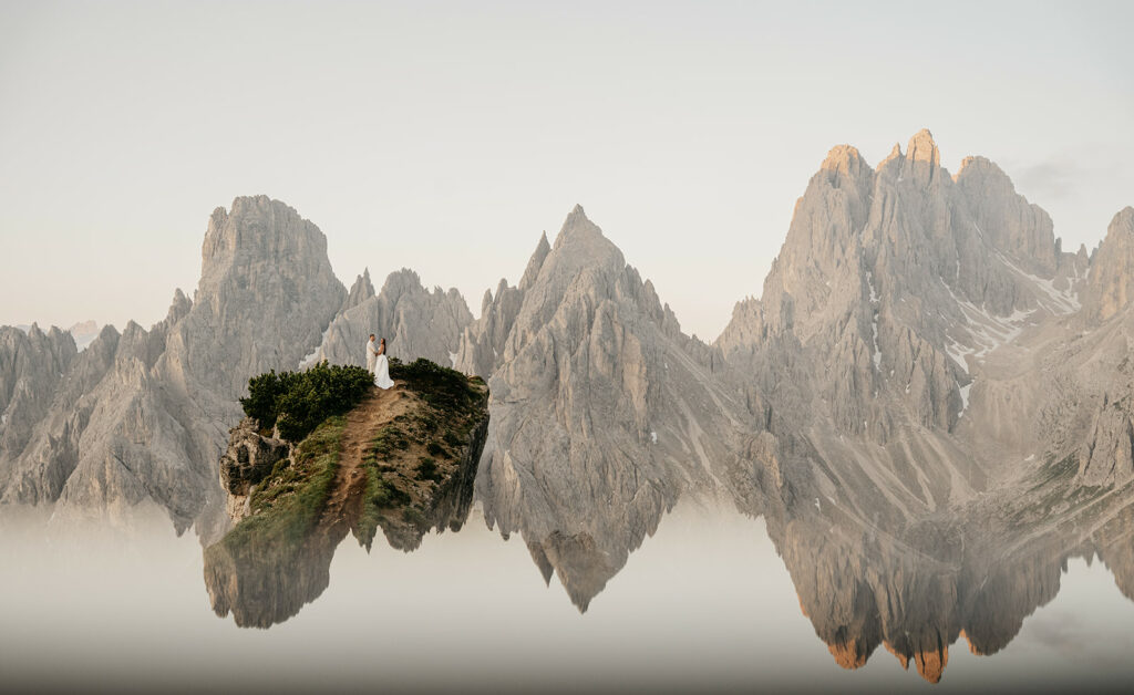 Couple on mountain peak surrounded by rugged cliffs.