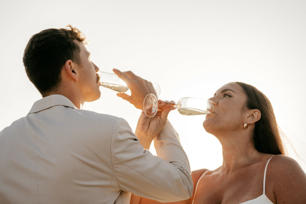 Couple toasting with champagne glasses outdoors at sunset.