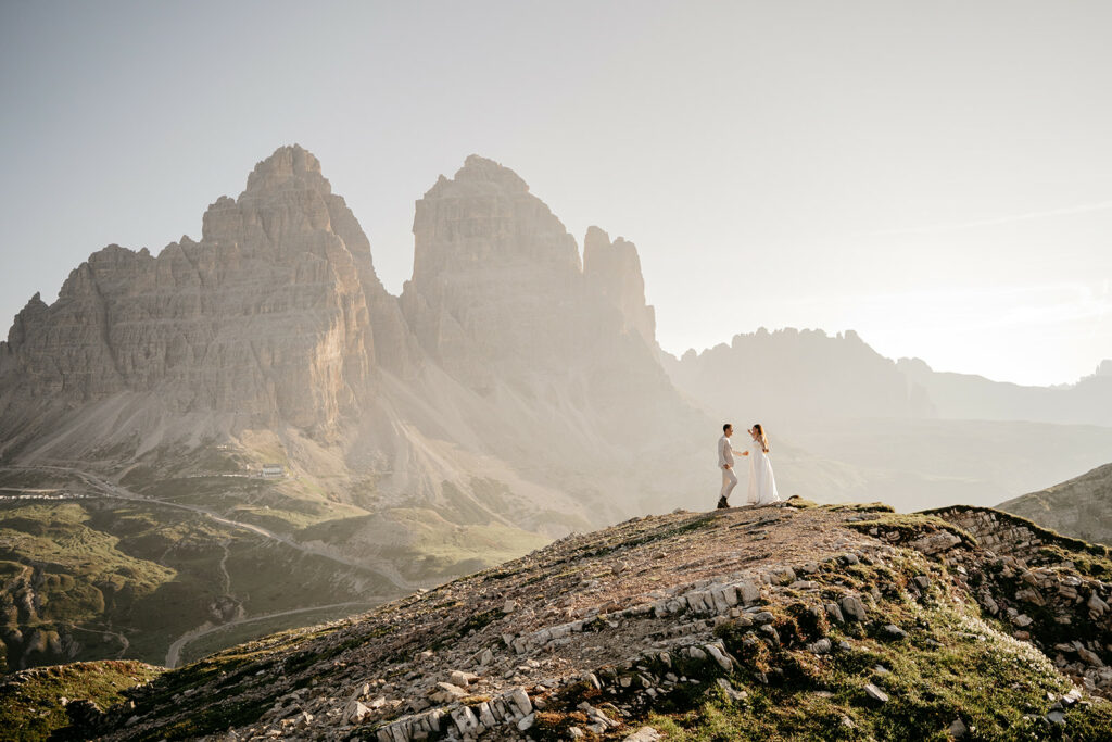 Couple stands on mountain with dramatic scenery backdrop.