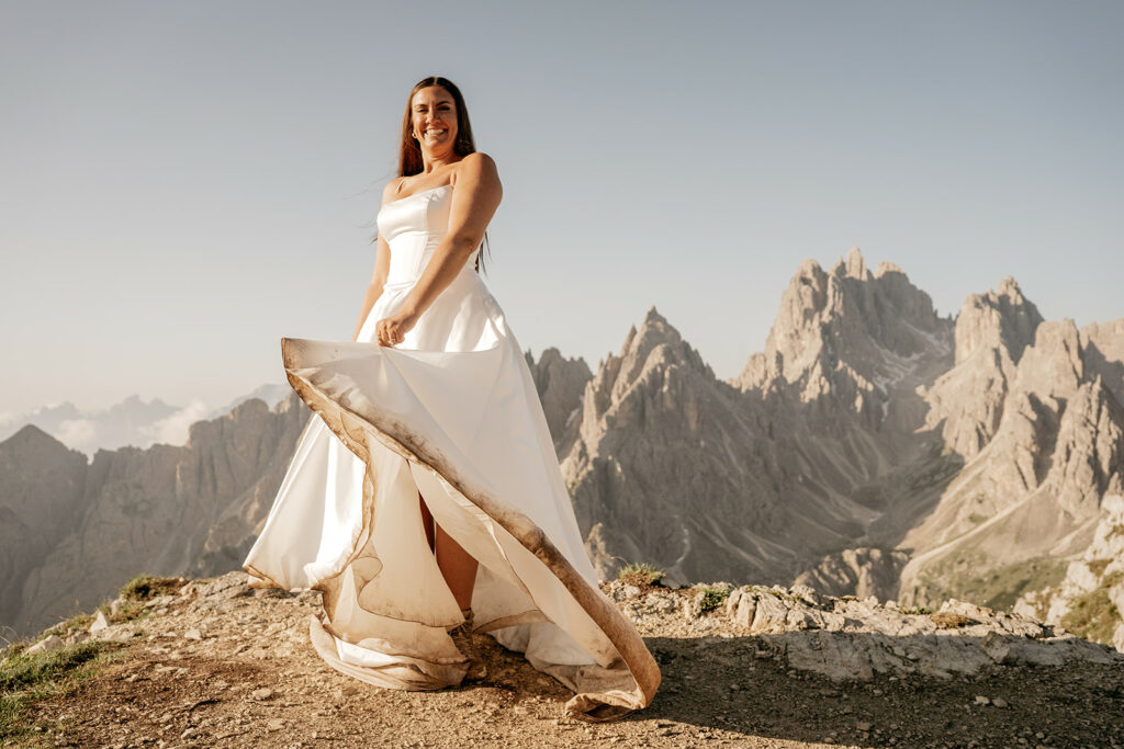 Bride on mountain, holding dress, smiling
