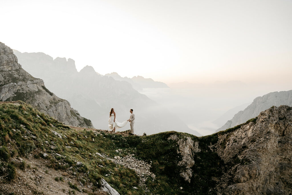 Couple in wedding attire on mountain cliff.