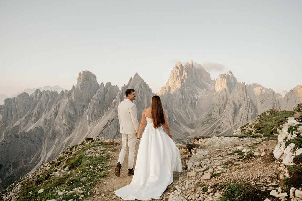 Couple holds hands on mountain trail at sunrise.