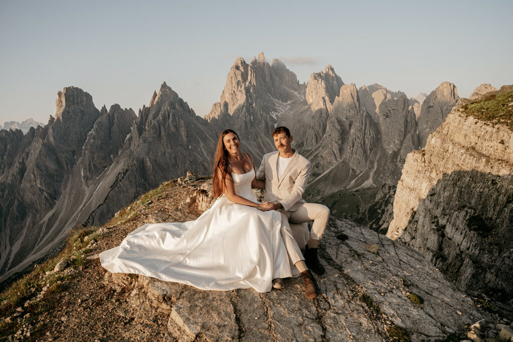 Couple in wedding attire on mountain cliff.