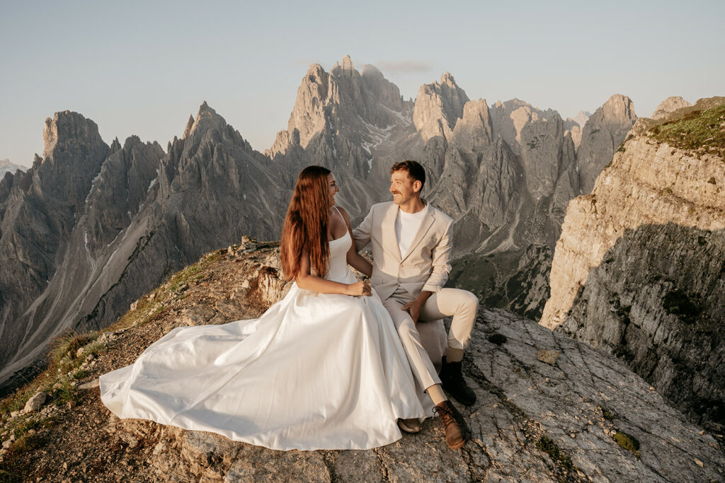 Couple in wedding attire on mountain cliff.