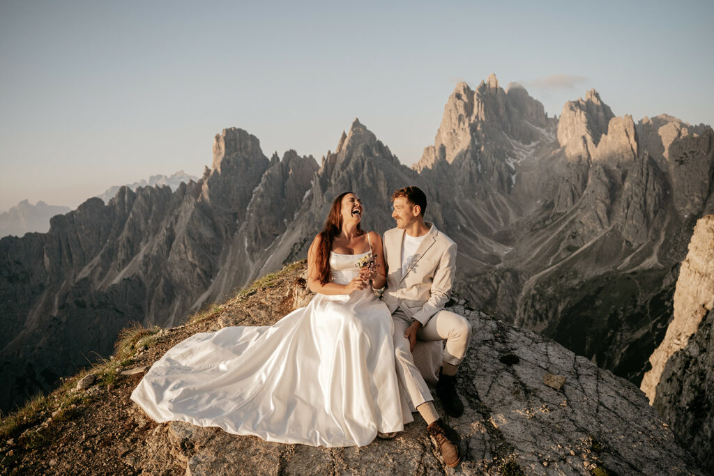 Couple in wedding attire on mountain cliff.
