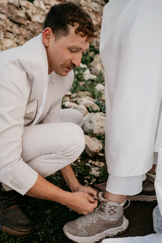 Man ties shoelaces on another's sneaker outdoors.