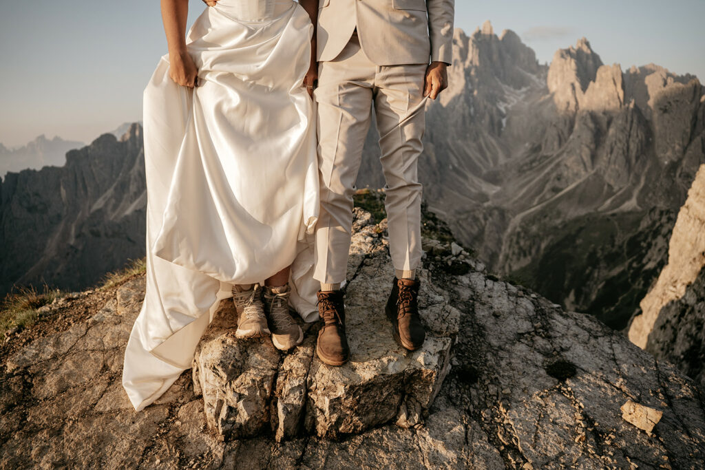 Bride and groom in hiking boots on mountain cliff.