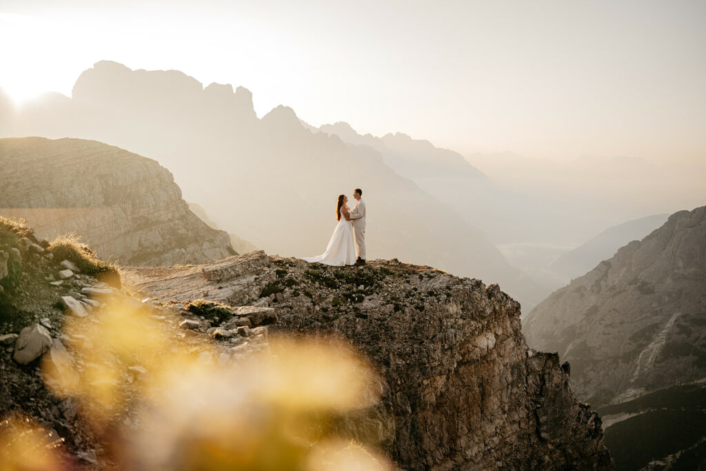 Couple embraces on mountain cliff at sunset.