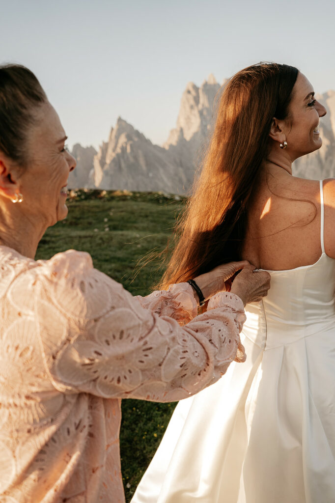Woman helps bride with dress outdoors