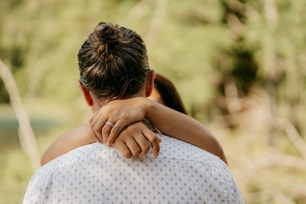 Engagement embrace outdoors with engagement ring visible.