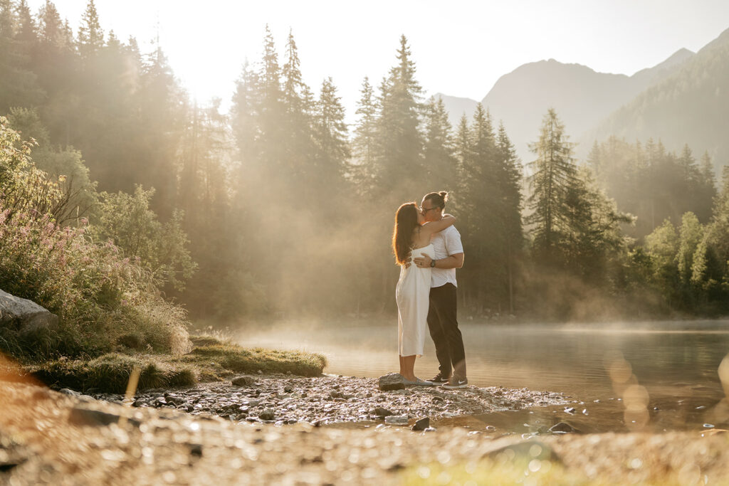 Couple embraces by a serene lakeside at sunset.