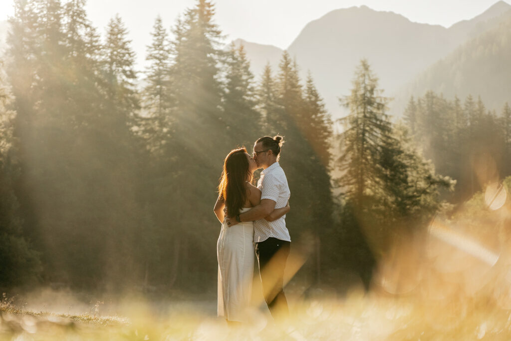 Couple kissing in sunlit forest landscape.
