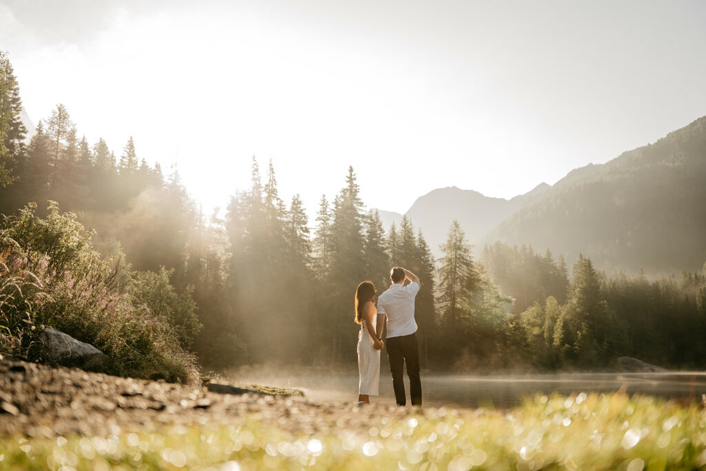 Couple enjoying misty forest sunrise by a lake.