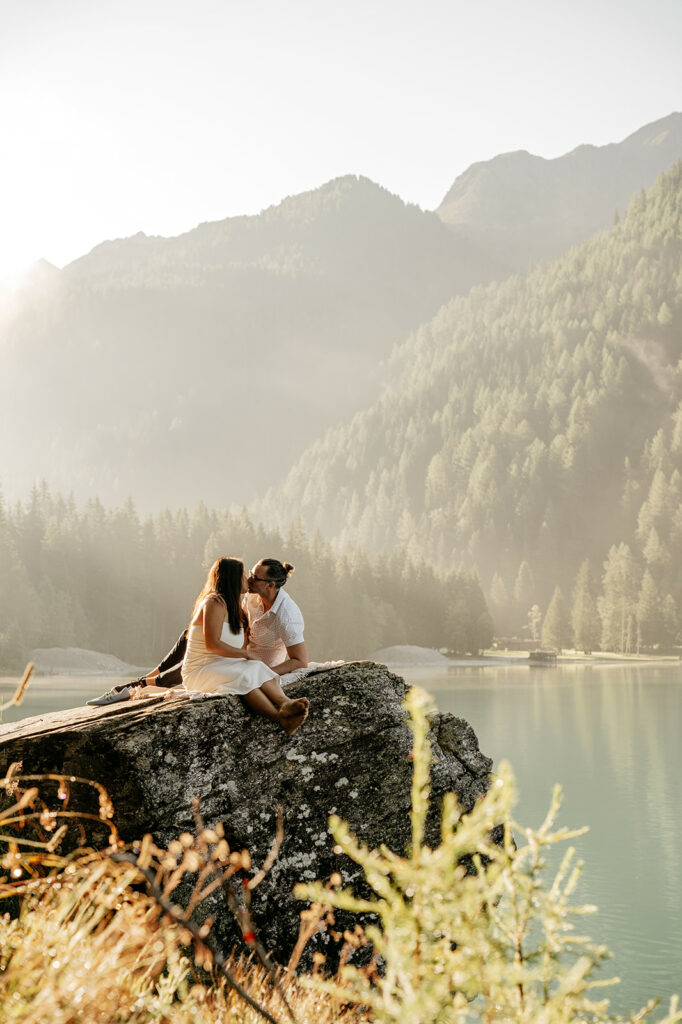 Couple kissing on rock by serene lake.