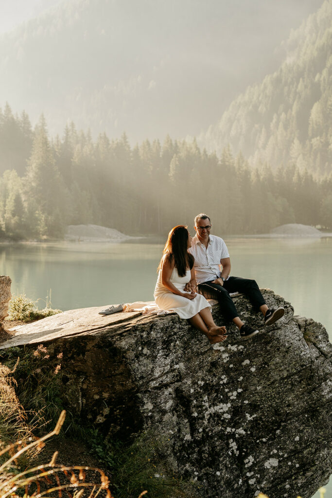 Couple sitting on rock by mountain lake.