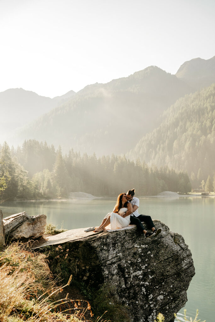 Couple embraces on lake rock, misty mountain backdrop.