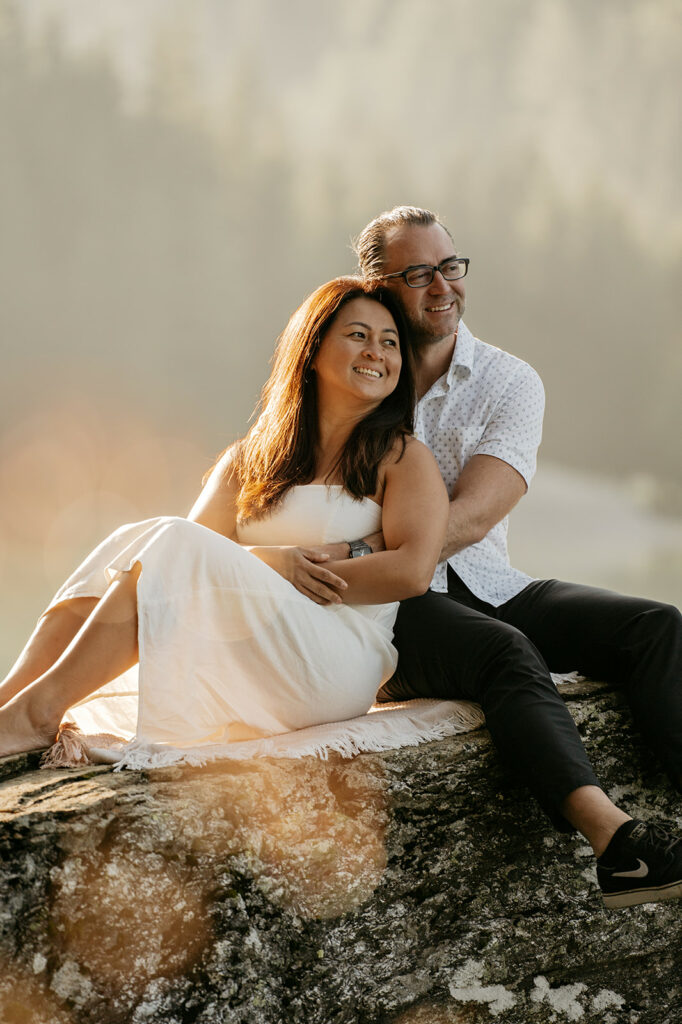 Couple sitting on rock, smiling in sunlight.