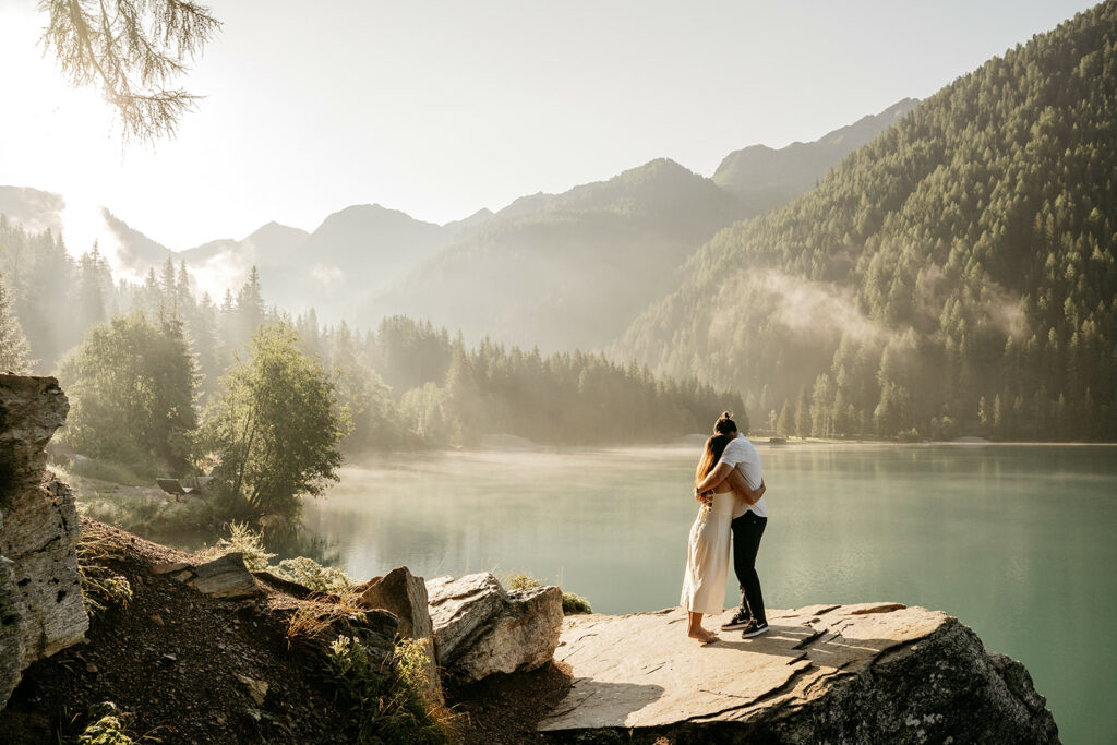 Couple hugging by serene mountain lake at sunrise.
